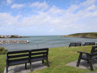 A grassy area with black benches overlooking a body of water and a small harbor with boats at Monfa in Cemaes Bay