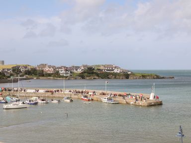 A harbor with boats and people on a pier in front of a coastal village at Monfa in Cemaes Bay