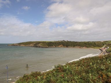 A coastal bay with a curved shoreline a road along the coast and grassy hills in the background at Monfa in Cemaes Bay
