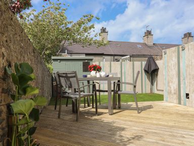 An outdoor patio with a wooden deck table and four chairs a flowerpot on the table a small shed and a fenced yard at Monfa in Cemaes Bay