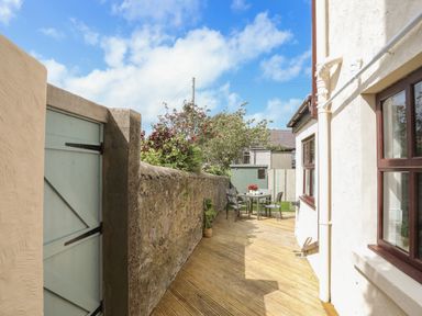 A wooden decked patio area with a stone wall a green gate a table with four chairs and a small garden shed at Monfa in Cemaes Bay