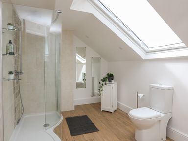 A bathroom with a shower, toilet, small cabinet, two mirrors, and a skylight at Monfa in Cemaes Bay