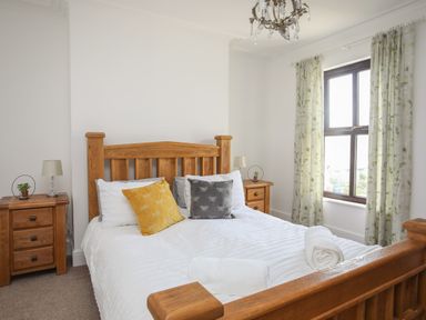 A bedroom with a wooden bed white bedding yellow and gray pillows two bedside tables with lamps and plants floral curtains at Monfa in Cemaes Bay