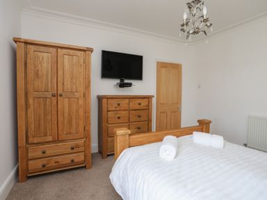 A bedroom with wooden wardrobe and dresser a wall-mounted TV and a bed with rolled white towels at Monfa in Cemaes Bay