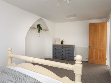 A bedroom with a cream bed frame gray dresser with a mirror and flowers and a wooden door at Monfa in Cemaes Bay
