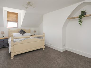 A bedroom with a cream wooden bed, two bedside tables with lamps, a window with blinds and a wooden shelf with a plant at Monfa in Cemaes Bay