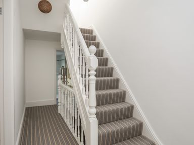 A staircase with a striped carpet and white banister in a hallway at Monfa in Cemaes Bay