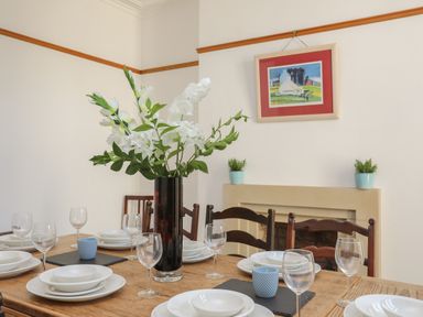 Dining table set with white plates bowls wine glasses and a vase with white flowers in a room with chairs a fireplace and wall art at Monfa in Cemaes Bay