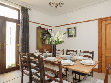 A dining room with a wooden table set with plates glasses and a vase of flowers at Monfa in Cemaes Bay