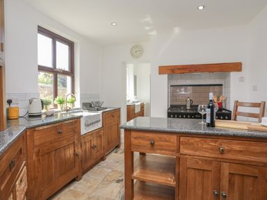 A kitchen with wooden cabinets a window with plants a stove and a countertop with a wine bottle and glass at Monfa in Cemaes Bay