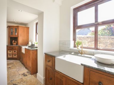 A kitchen with wooden cabinets a large white sink and a window overlooking a stone wall at Monfa in Cemaes Bay