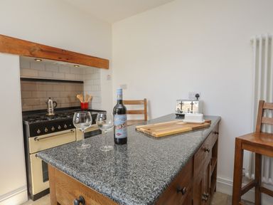 A kitchen with a stove, wooden cabinets, a bottle and two wine glasses on the countertop at Monfa in Cemaes Bay