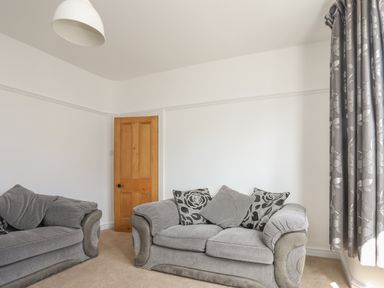 A living room with two grey sofas a wooden door and grey floral curtains at Monfa in Cemaes Bay