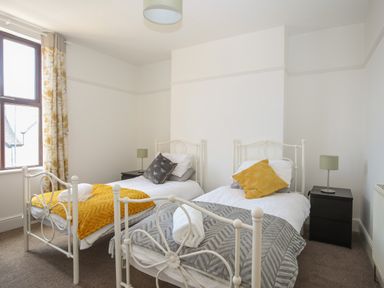 A bedroom with two single beds white metal frames side tables lamps and a window with curtains at Monfa in Cemaes Bay