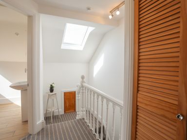 A landing with striped carpet a white balustrade a wooden door and a pedestal table with a vase and flowers at Monfa in Cemaes Bay