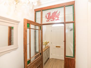 A hallway with a wooden door with textured glass a white door a cabinet with flowers and a mirror at Monfa in Cemaes Bay