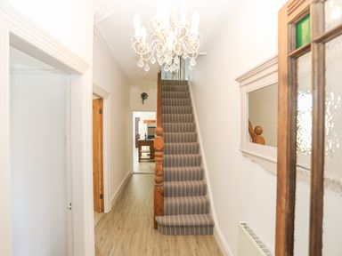 A hallway with striped carpeted stairs a wooden banister a chandelier a wall mirror and doorways leading to other rooms at Monfa in Cemaes Bay
