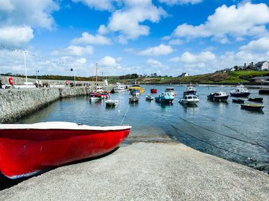 A harbor with boats docked in the water and a red boat on the concrete edge at Monfa in Cemaes Bay