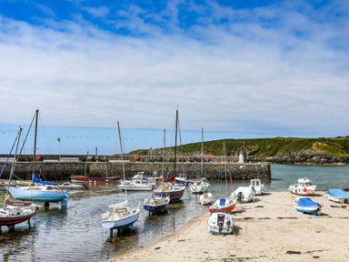 A harbor with boats anchored in water and on the sandy shore near a stone pier and green hills at Monfa in Cemaes Bay