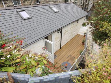 An outdoor patio with wooden decking chairs and a table outside a stone house at Glan Meon Cottage in Barmouth