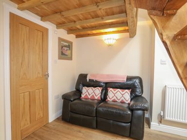A small living area with a black leather sofa two patterned cushions a pink throw blanket a wooden door wooden ceiling beams and stairs at Glan Meon Cottage in Barmouth