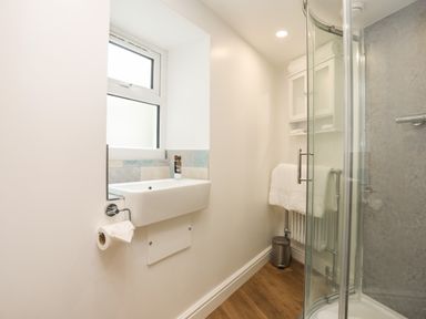 A bathroom with a sink under a window and a glass shower enclosure at Glan Meon Cottage in Barmouth