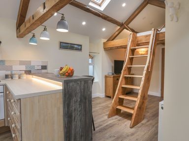 A kitchen area with a wooden counter and fruit bowl next to wooden stairs leading to a loft at Glan Meon Cottage in Barmouth