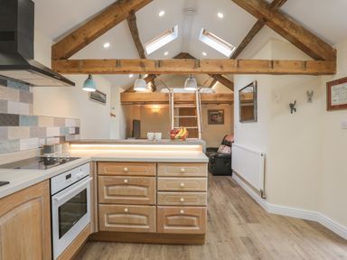 A kitchen area with wooden cabinets and an oven under exposed wooden beams at Glan Meon Cottage in Barmouth