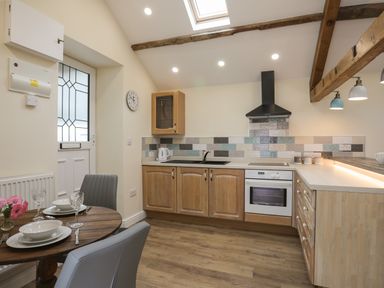 A kitchen with wooden cabinets a dining table with place settings and exposed ceiling beams at Glan Meon Cottage in Barmouth