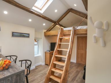A room with wooden loft bed accessed by a wooden ladder a TV on a wooden cabinet stools by a counter and a bowl of fruit at Glan Meon Cottage in Barmouth