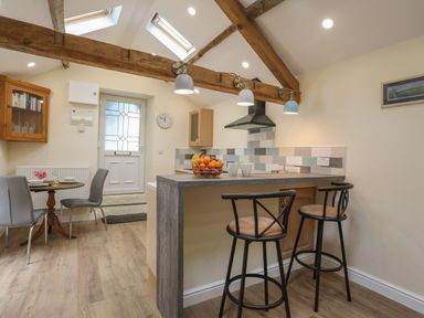 A kitchen with a breakfast bar and two stools a small dining table with two chairs and a door at Glan Meon Cottage in Barmouth