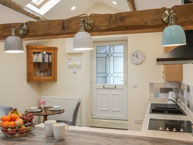A kitchen with a wooden table with fruit basket and cups and a dining table set for two at Glan Meon Cottage in Barmouth