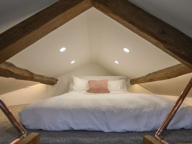 A small attic bedroom with a bed white bedding a pink pillow wooden beams and recessed ceiling lights at Glan Meon Cottage in Barmouth