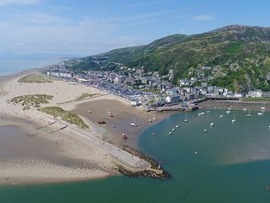 A coastal town with a beach harbor boats and hills in the background at Glan Meon Cottage in Barmouth