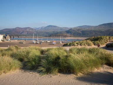 A sandy beach with grass dunes boats on the shore and mountains in the background at Glan Meon Cottage in Barmouth