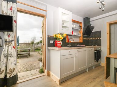 A kitchen with cabinets sink stovetop and open door leading to outdoor seating at Tiny Willow in Farrington near Child Okeford