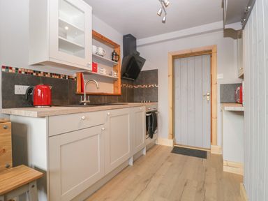 A kitchen with cabinets a stove a sink and a red kettle at Tiny Willow in Farrington near Child Okeford