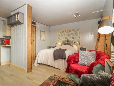 A bedroom with a double bed a red covered armchair a wooden pillar and a small kitchen area at Tiny Willow Farrington near Child Okeford