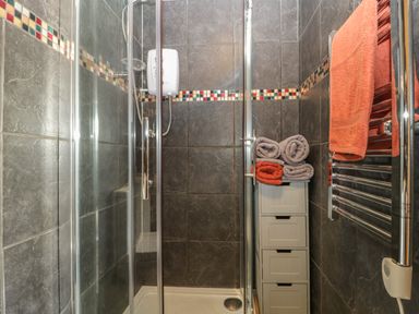A small shower area with glass doors dark tiled walls a white storage unit with rolled towels and a heated towel rail at Tiny Willow in Farrington near Child Okeford