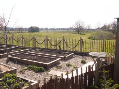A garden with raised planting beds a gravel path and a round wooden table beyond a wooden fence at Tiny Willow in Farrington near Child Okeford