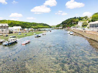 A river with small boats docked along the banks and buildings on both sides at Bay Tree Cottage in West Looe