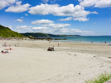 A sandy beach with people sunbathing and walking near the water at Bay Tree Cottage in West Looe