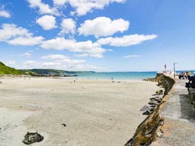 A sandy beach with people walking near the shore and a rocky sea wall with people standing on it at Bay Tree Cottage in West Looe