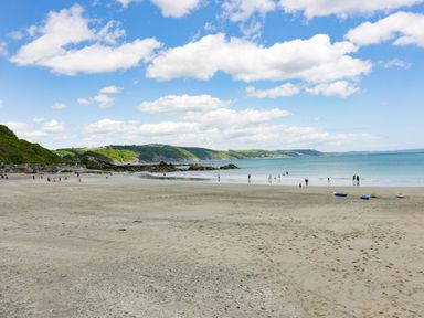 A sandy beach with people near the water and hills in the background at Bay Tree Cottage in West Looe