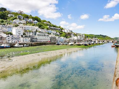 A river with boats docked along the banks and houses on a hillside at Bay Tree Cottage in West Looe