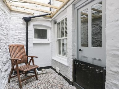 A small enclosed patio with a wooden chair gravel floor and a grey door at Bay Tree Cottage in West Looe