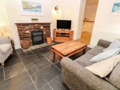 A living room with a gray sofa wooden coffee table stone fireplace and television stand at Bay Tree Cottage in West Looe
