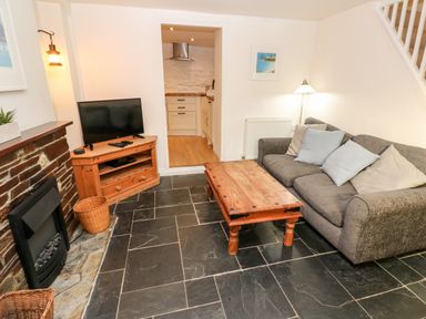 A living room with a gray sofa and wooden coffee table near a brick fireplace and television at Bay Tree Cottage in West Looe