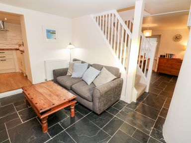 A small living area with a gray sofa and wooden coffee table near white stairs and wooden furniture at Bay Tree Cottage in West Looe