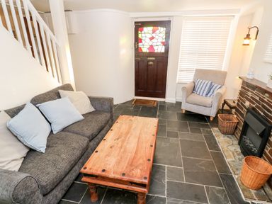 A sitting room with a grey sofa and armchair a wooden coffee table stained glass door and a fireplace at Bay Tree Cottage in West Looe